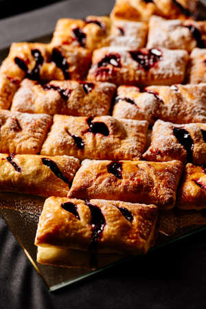 Sweet puff buns with jam sprinkled with powdered sugar on black backgroundの写真素材