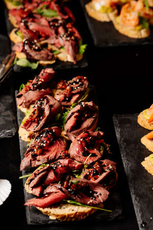 Bruschetta with baked beef, arugula and balsamic sauce on black tableの写真素材