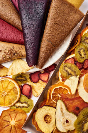 Close-up mix sliced dried fruits in craft paper box and mix fruit pastille marshmallow in white plate. Vegetarian lifestyle.の写真素材