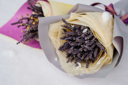Beautiful bouquet of lavender in yellow-purple packaging and bouquet of lavender in gray and yellow packaging on white snowの写真素材