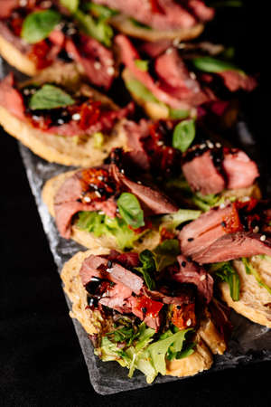 Bruschetta with baked beef, arugula and balsamic sauce on black tableの写真素材