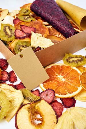 Scattered mix dried fruits and mix fruit pastille marshmallow in open craft paper square box on white background. Vegetarian lifestyle.の写真素材