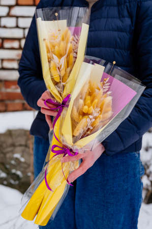 Two small beautiful bouquet of lagurus in transparent and yellow-purple packaging in hands of womanの写真素材