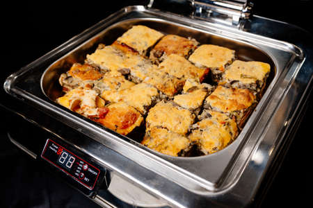 Silver color steam table of delicious portioned hot lasagne on black backgroundの写真素材