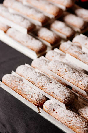 Tasty vanilla eclairs individually wrapped sprinkled with powdered sugar on black tableの写真素材