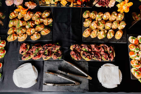 Various tasty bruschetta on black table with white napkins and kitchen tongs