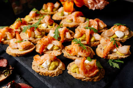 Bruschetta with fried shrimps, arugula and cheese sauce on black tableの写真素材