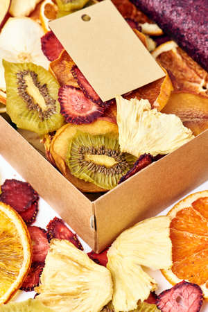 Scattered mix dried fruits and mix fruit pastille marshmallow in open craft paper square box on white background. Vegetarian lifestyle.の写真素材