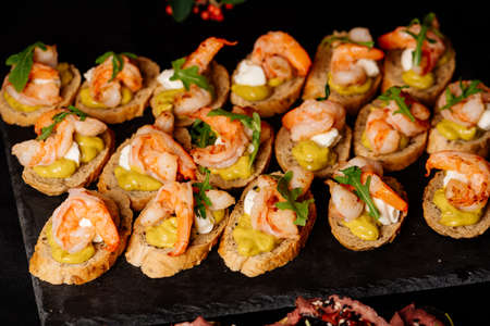 Bruschetta with fried shrimps, arugula and cheese sauce on black tableの写真素材