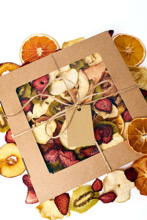 Mix dried fruits in craft paper square box with transparent lid with twine ribbon on scattered mix dried fruits background on white background. Vegetarian lifestyle.の写真素材
