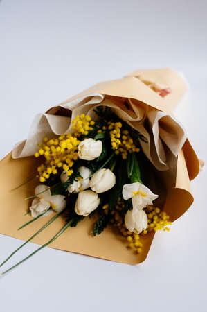 Bouquet of white tulips, narcissus and mimosa in beige package on white background.の写真素材