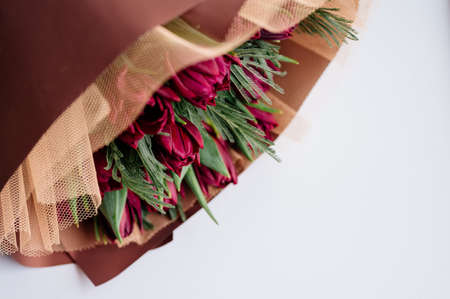 Bouquet of red tulips and mimosa leaves in burgundy package on white background.の写真素材