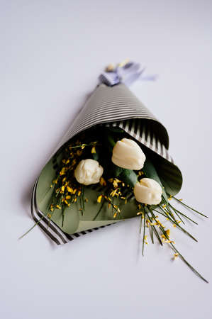 Bouquet of white tulips in striped black and pistachio-colored package on white background.の写真素材