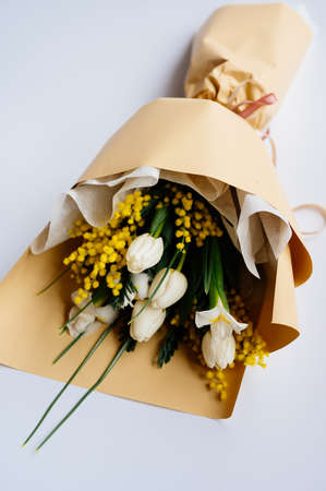 Bouquet of white tulips, narcissus and mimosa in beige package on white background.の写真素材