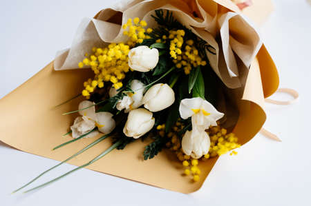 Bouquet of white tulips, narcissus and mimosa in beige package on white background.の写真素材