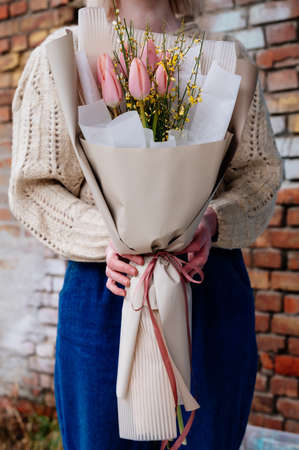Bouquet of pink tulips in beige package in the hands of girl florist in knitted pullover on brick wall background.の写真素材
