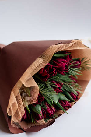 Bouquet of red tulips and mimosa leaves in burgundy package on white background.の写真素材