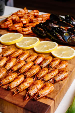 Delicious fried prawns and yummy fried mussels in shells with creamy sauce and herbs and tasty fried langoustines and sliced yellow juicy lemon on wooden cutting boardの写真素材