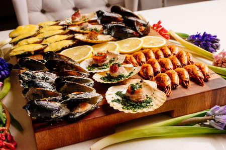 Delicious fried and baked mussels in shells with creamy sauce and herbs and baked scallops in shell with bacon and herbs and sliced yellow juicy lemon on wooden cutting board with black card on white background with pink and purple hyacinthsの写真素材