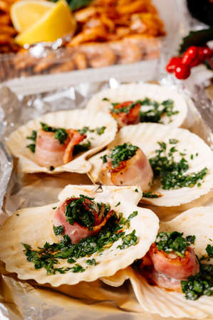 Luxury sea scallop in shell with bacon and herbs close-up. In background are red berries and fried large shrimps.の写真素材