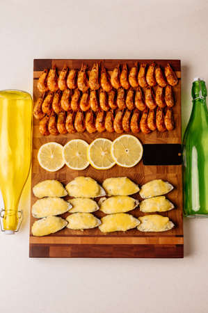 Appetizing mussels in shell baked with cheese sauce and sliced yellow juicy lemon and delicious fried shrimps on wooden cutting board with black card on white background with green and yellow glass bottlesの写真素材