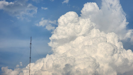 Blue sky with white clouds and a mobile phone antenna, background.