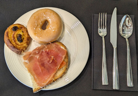 sweet and savory breakfast consisting of a donut, a spiral raisin danish and bread with ham and...