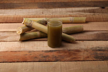 Sugarcane juice in glass with piece of sugarcane on wooden tableの写真素材