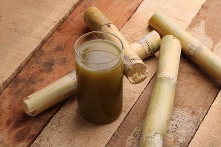 Sugarcane juice in glass with piece of sugarcane on wooden tableの写真素材