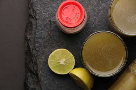 Sugarcane juice in glass with piece of sugarcane, lemon and black salt on wooden tableの写真素材