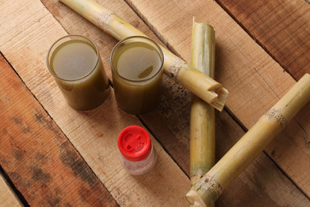 Sugarcane juice in glass with piece of sugarcane and black salt on wooden tableの写真素材