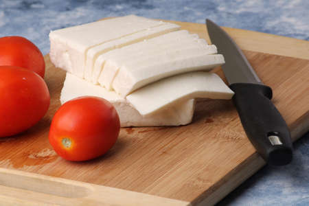 sliced fresh paneer or cottage cheese with tomatoes and knife on cutting board.の写真素材