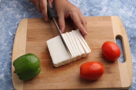 Paneer or cottage cheese with tomatoes, capsicum  and a knife on a wooden cutting Board.