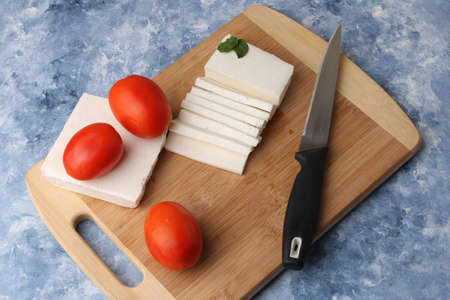 sliced fresh paneer or cottage cheese with tomatoes and knife on cutting board.の写真素材