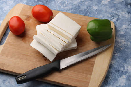 Paneer or cottage cheese with tomatoes, capsicum  and a knife on a wooden cutting Board.の写真素材