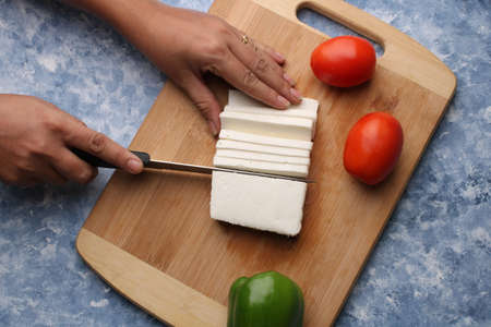 Paneer or cottage cheese with tomatoes, capsicum  and a knife on a wooden cutting Board.