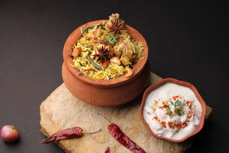Spicy chicken biryani in traditional handi or clay pot. served with onion raitaの写真素材