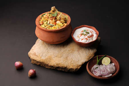 Spicy chicken biryani in traditional handi or clay pot. served with onion raita