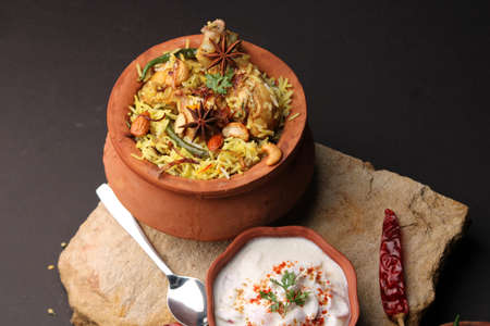 Spicy chicken biryani in traditional handi or clay pot. served with onion raitaの写真素材