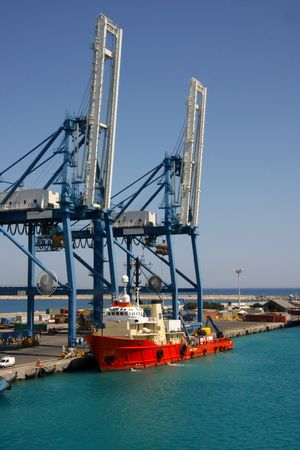 In the port Redd colored boat and container lifting cranes View on trading port with cranes and a red boat の写真素材