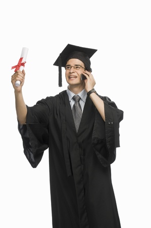 Happy male graduate holding his diploma and talking on a mobile phoneの写真素材