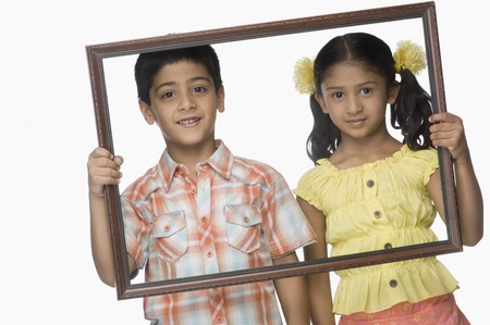 Portrait of a girl and a boy holding an empty picture frameの写真素材