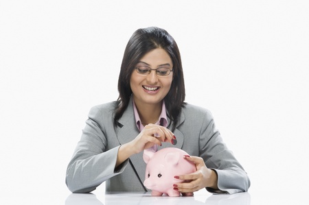 Businesswoman inserting a coin into a piggy bankの写真素材