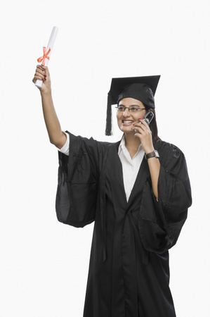 Graduate woman talking on a mobile phone and holding her diplomaの写真素材