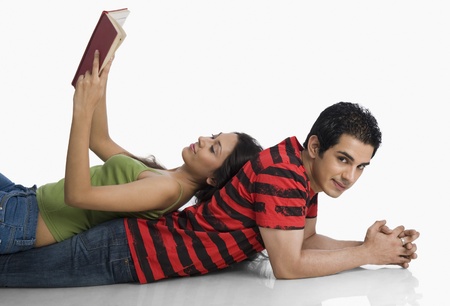 Woman lying on a man's back and reading a bookの写真素材