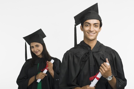 Couple in graduation gowns holding diplomas and smilingの写真素材