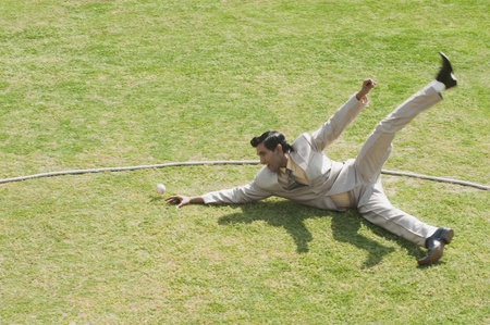 Businessman diving to stop a ball near boundary line in a cricket fieldの写真素材