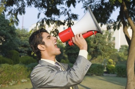 Businessman shouting into a megaphone in a parkの写真素材
