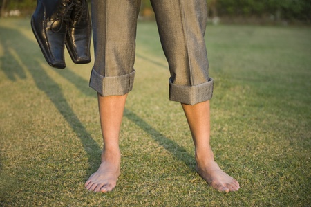 Low section view of a businessman holding shoes in a parkの写真素材