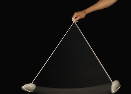 Close-up of a person's hand swinging a stone pendulum